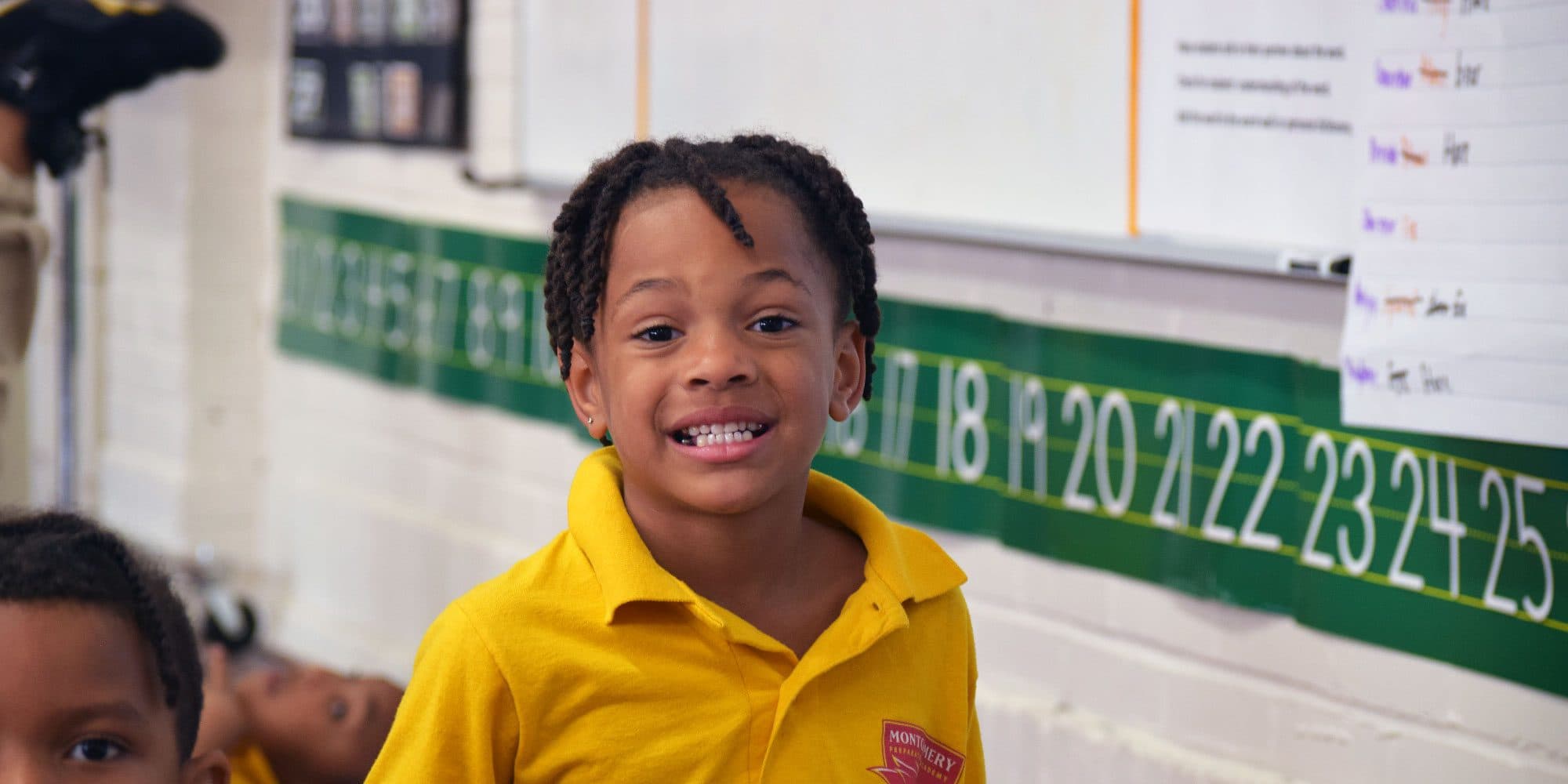 Smiling student in a yellow school shirt in a classroom.