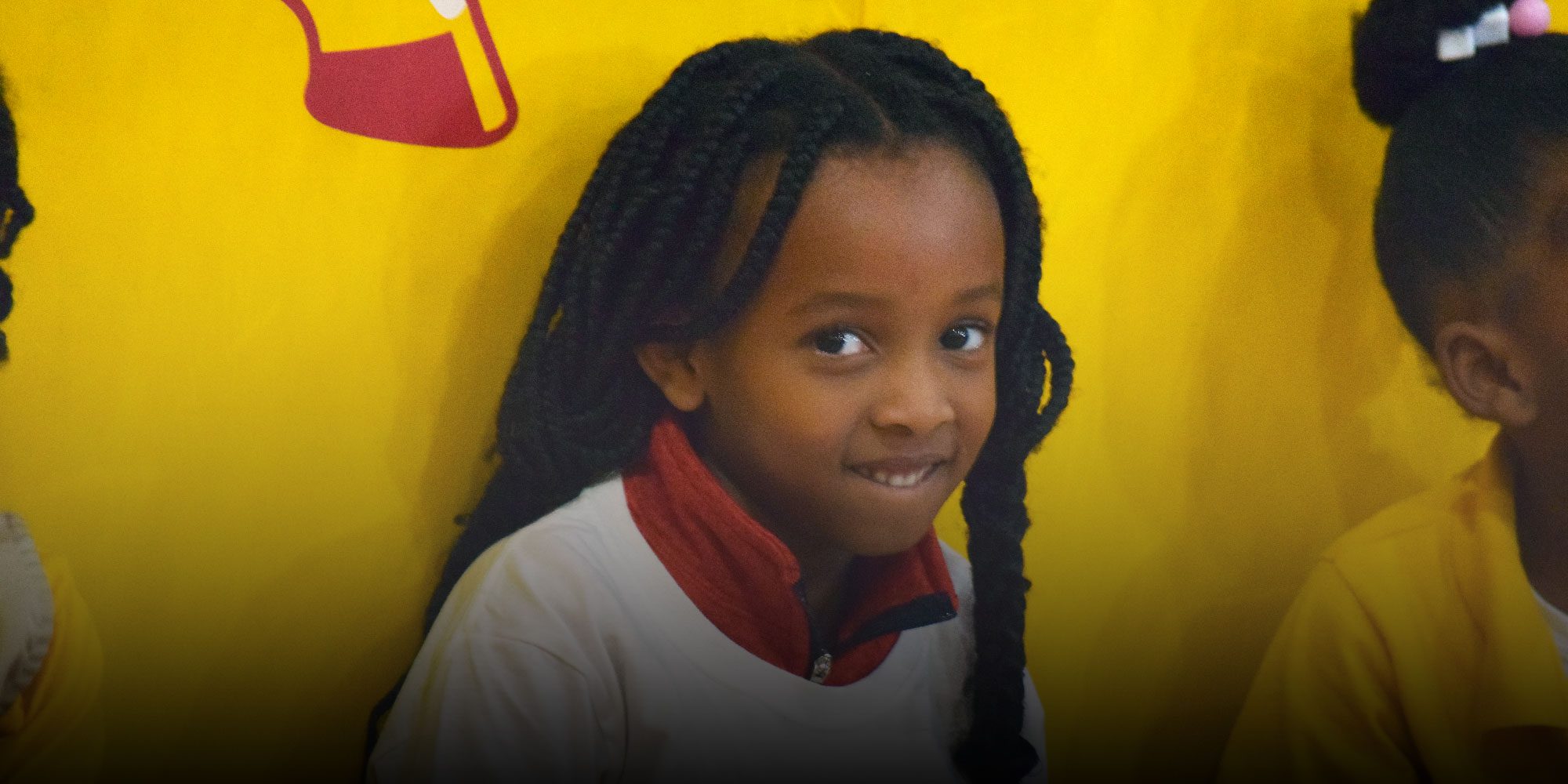 Smiling student with long braids in front of a yellow wall.